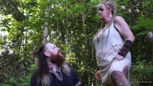 Jamie kneels before the Viking Queen in a forest