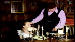 The master inspects his servant who kneels by the dining table