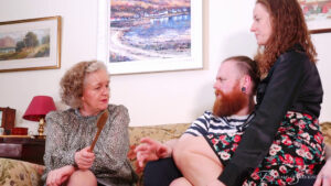 Matilda's aunt sits holding a wooden spoon as they all talk on the couch together