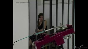 Pandora hugs herself whilst she sits in her cell, the spanking machine is in the foreground