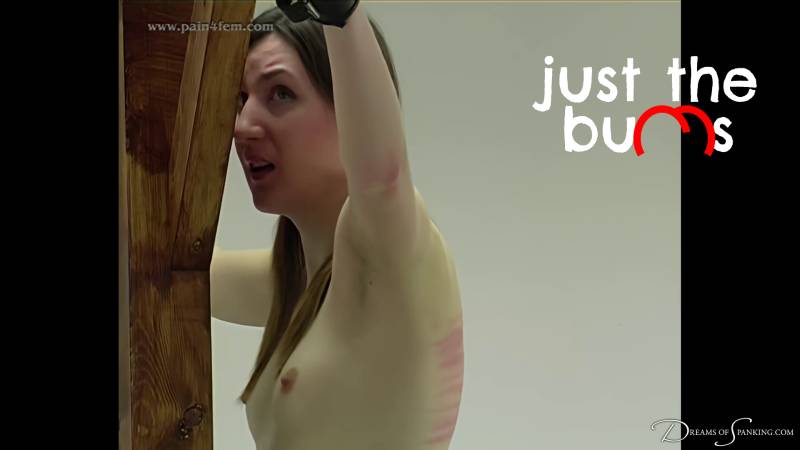 Pandora stands cuffed to a cross, her back exposed as she receives her machine whipping